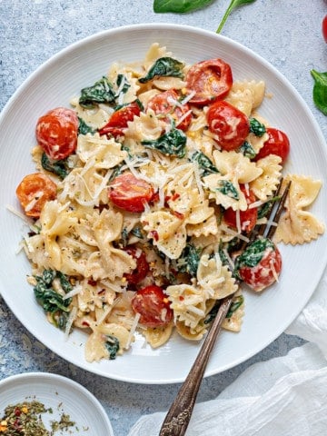 one white plate filled with spinach with tomatoes and pasta