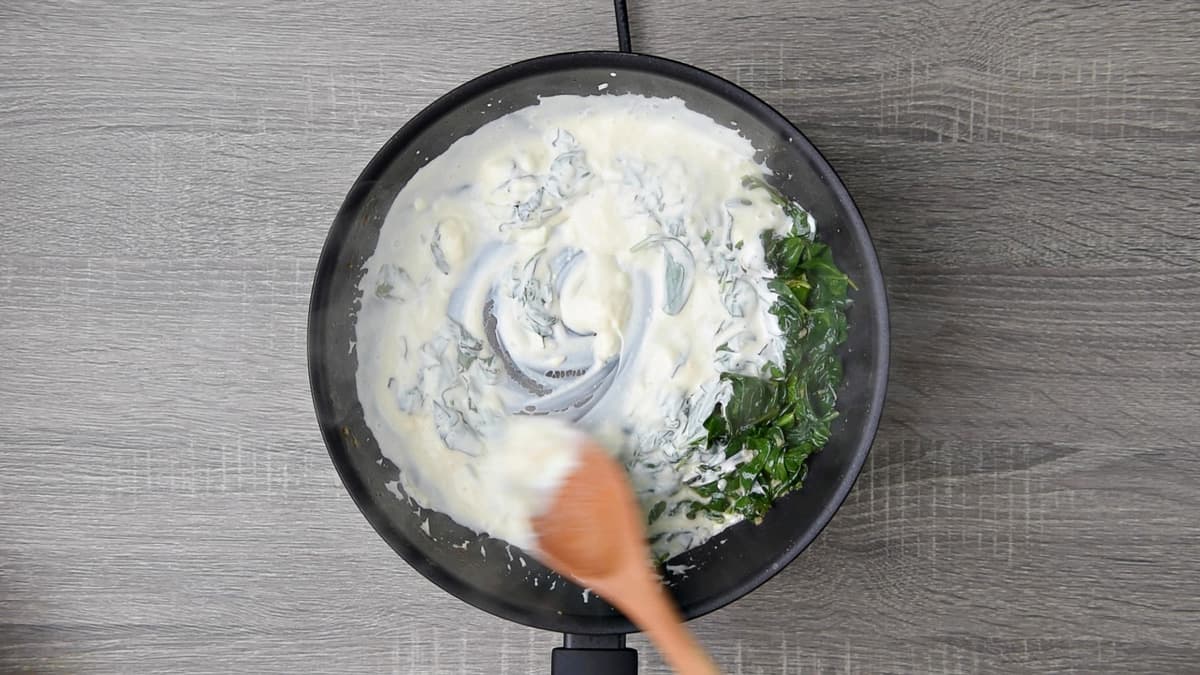 mixing cream cheese with fresh spinach with wooden spoon in skillet 
