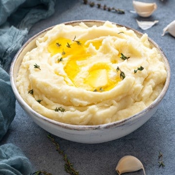 white bowl with fluffy mashed potatoes with roasted garlic, butter and herbs
