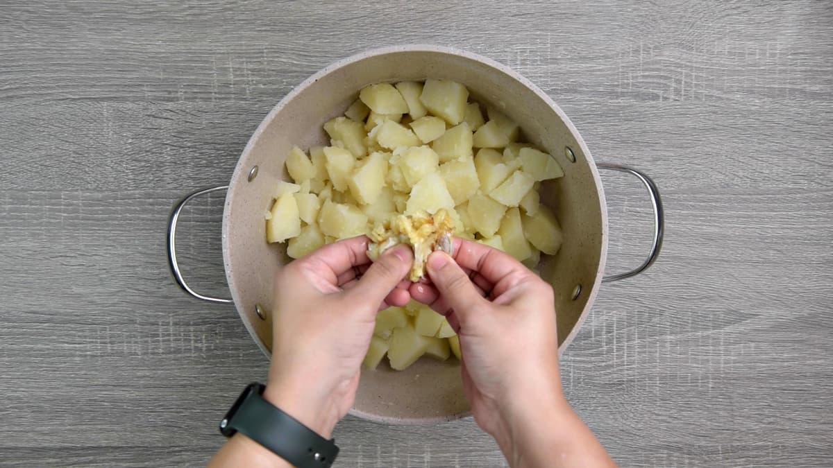 squeezing roasted garlic over potatoes in pot