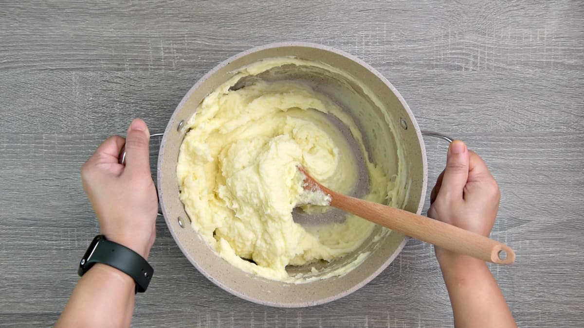 mixing fluffy mashed potatoes in pot with spoon