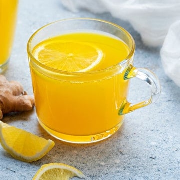two glass mugs with ginger turmeric tea on light blue table