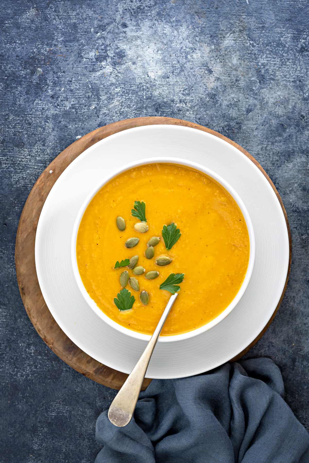 white bowl filled with butternut squash soup topped with parsley and pumpkin seeds