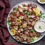 white plate with roasted red potatoes, lemon, parsley, pomegranate, and tahini sauce