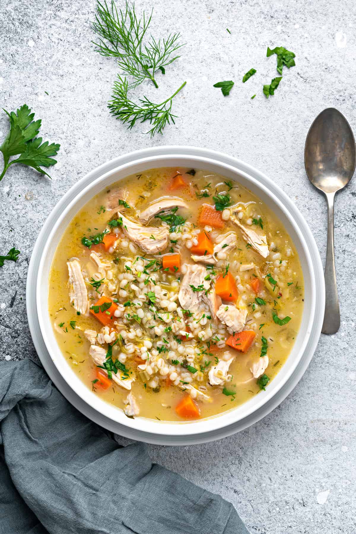 top view of chicken barley soup in bowl with fresh herbs and spoon on side.