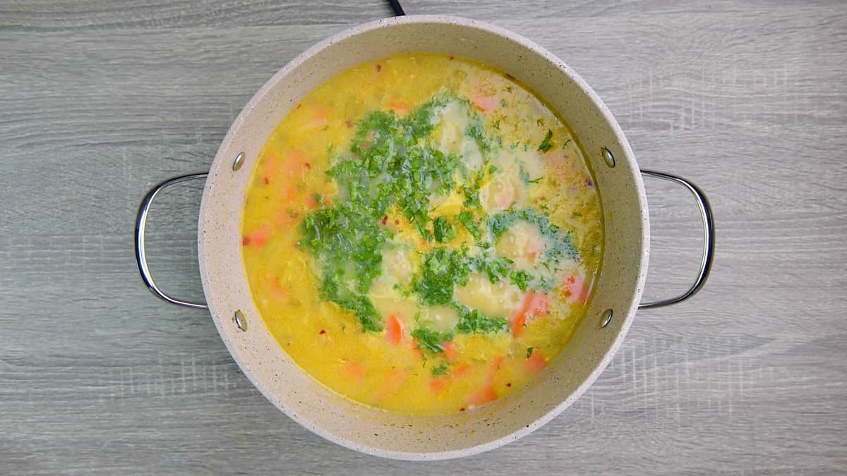 adding herbs to boiled chicken barley soup in pot.