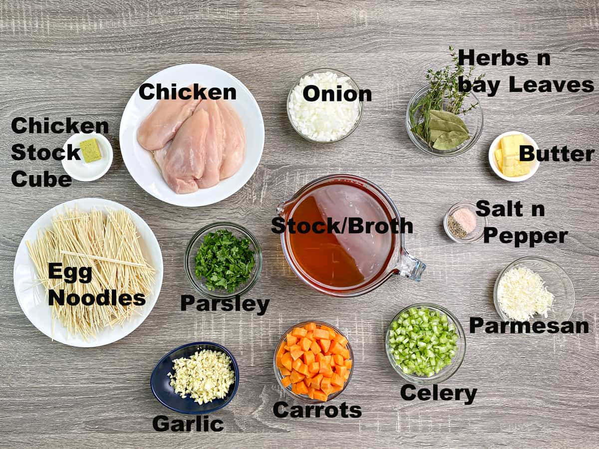 egg noodles, stock cube, chicken onion, celery, carrot, spices, herbs and seasonings, broth, parmesan, butter measured in bowls for noodle soup recipe