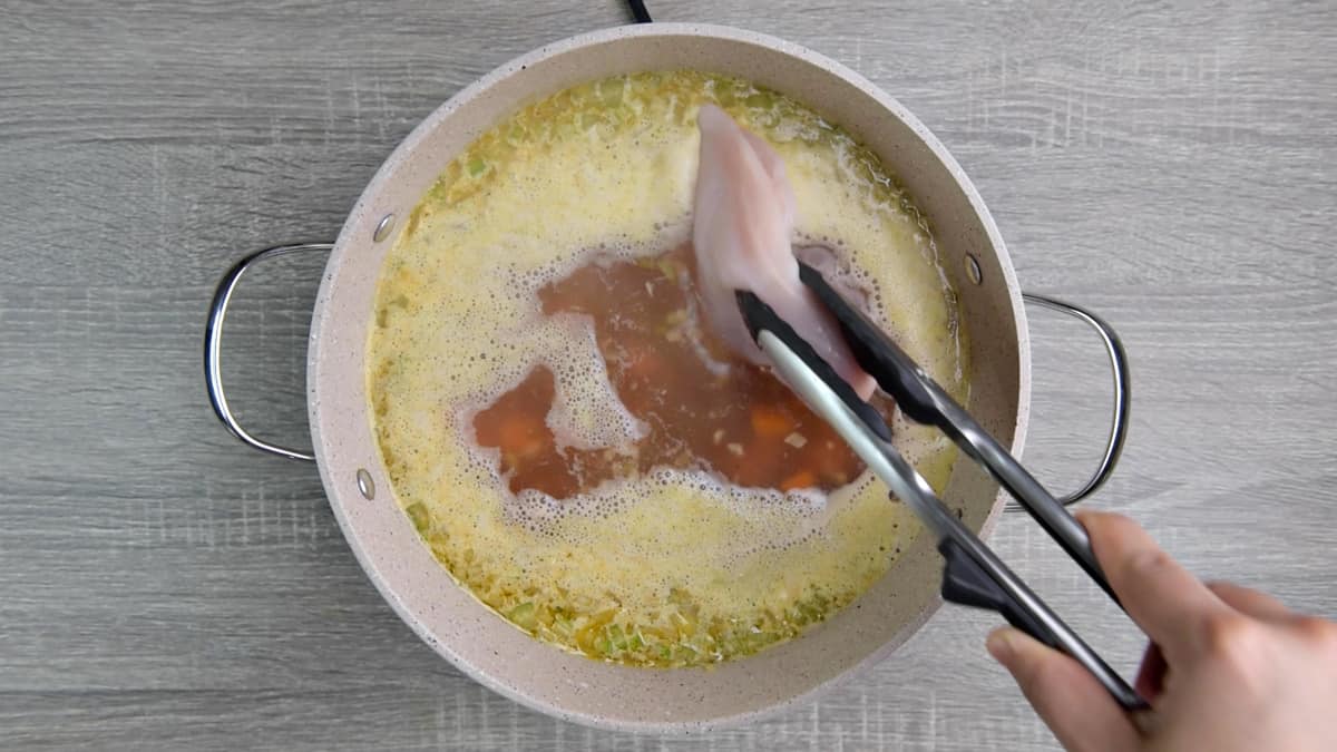 adding raw chicken breasts to the pot with broth 