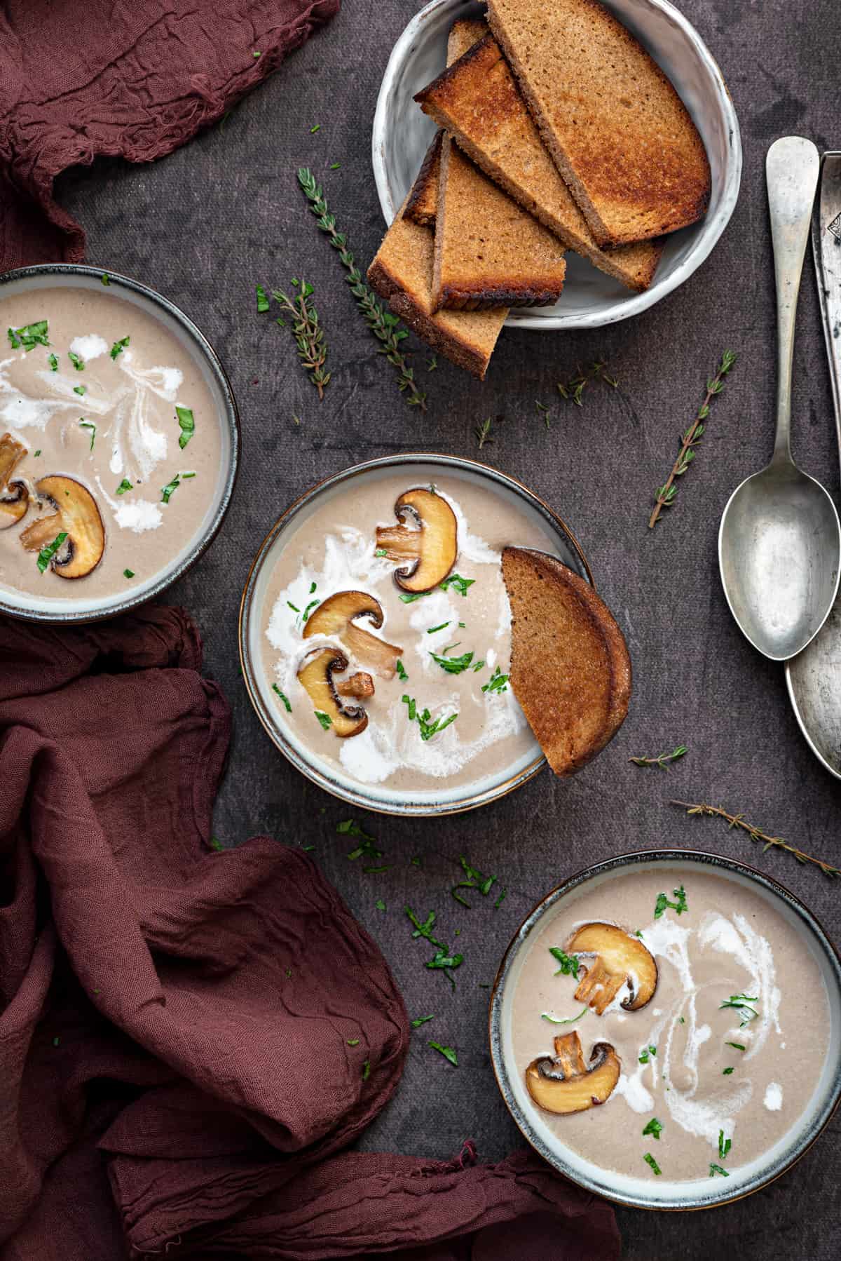 three bowls of cream of mushroom soup with herbs and toast
