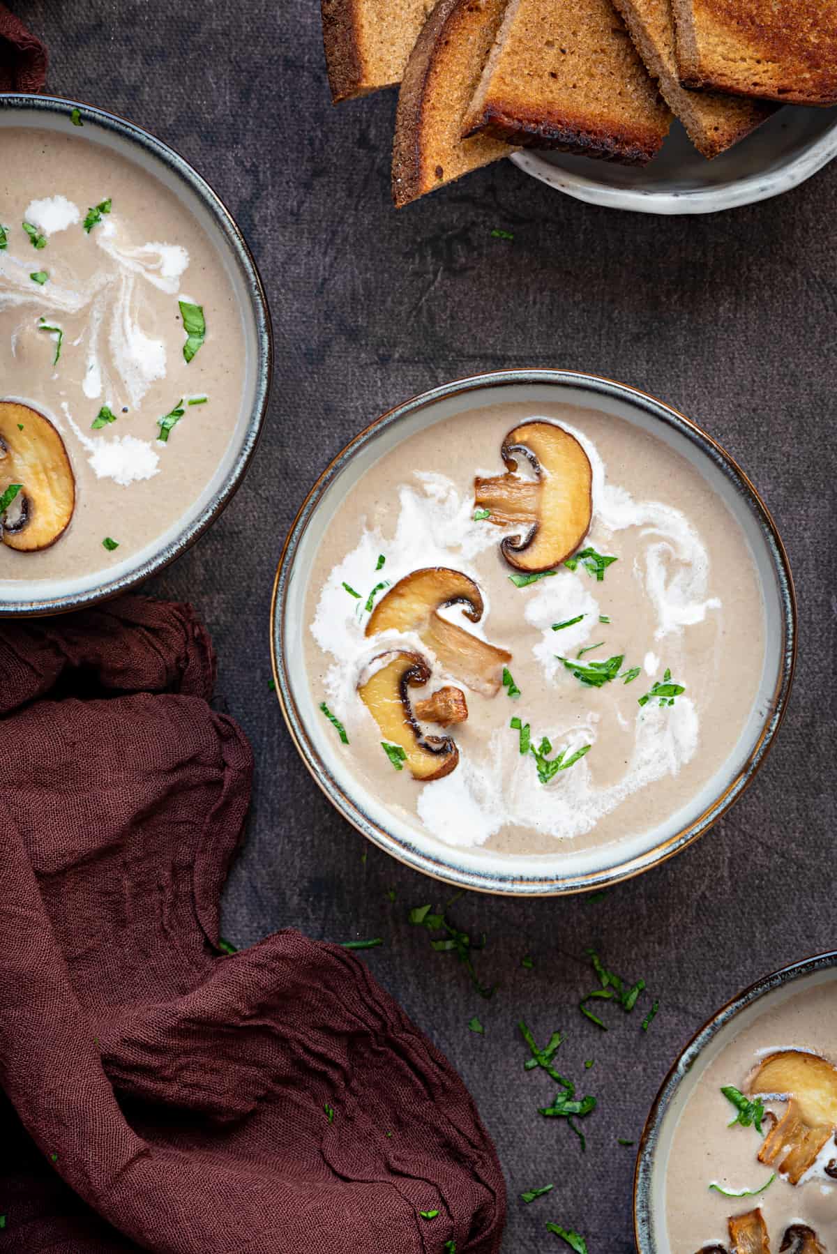 three bowls of cream of mushroom soup with roasted mushrooms, cream, and toast