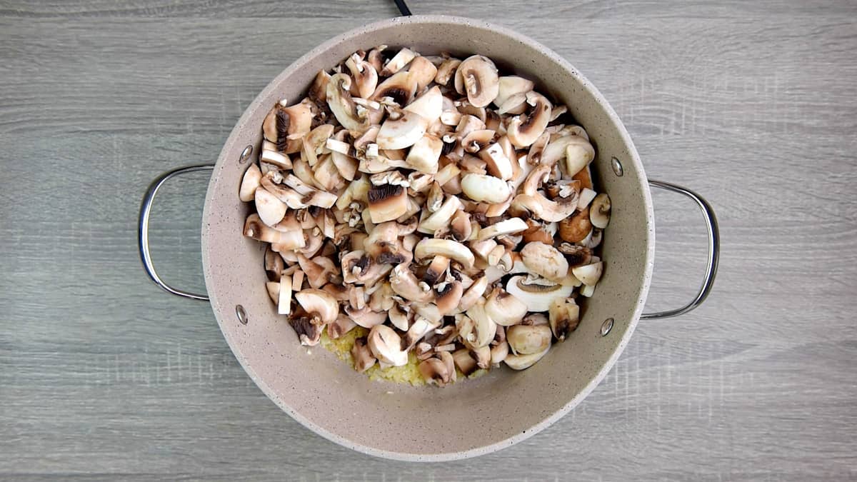 adding sliced mushrooms to pot of ingredients 