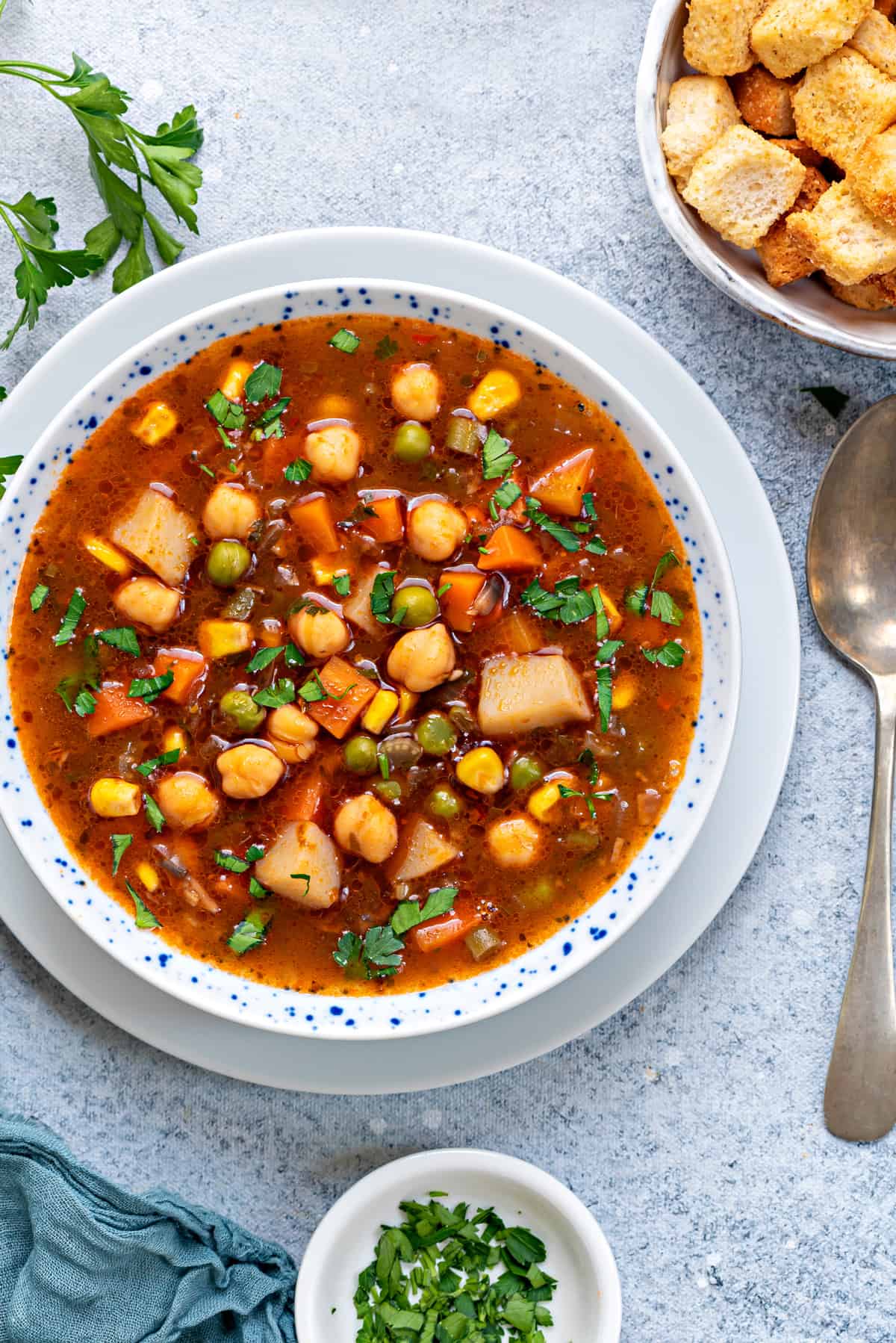 one bowl of vegetable soup on plate with spoon and croutons on side 