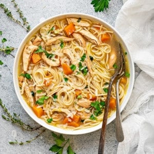 chicken noodle soup with carrots in white bowl with silverware