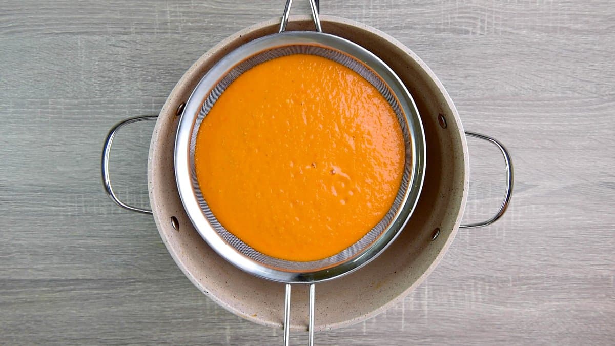 straining puréed tomato soup over pot 