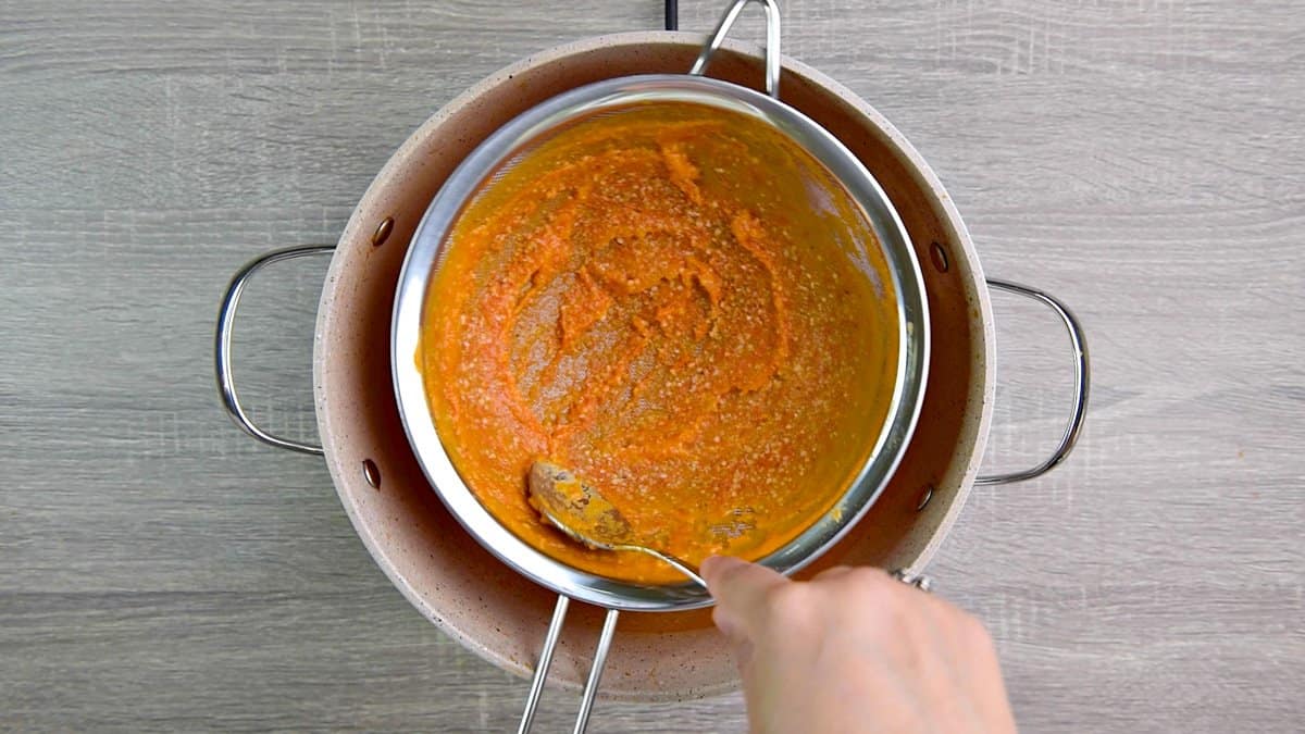 straining the pureed tomato soup over pot.