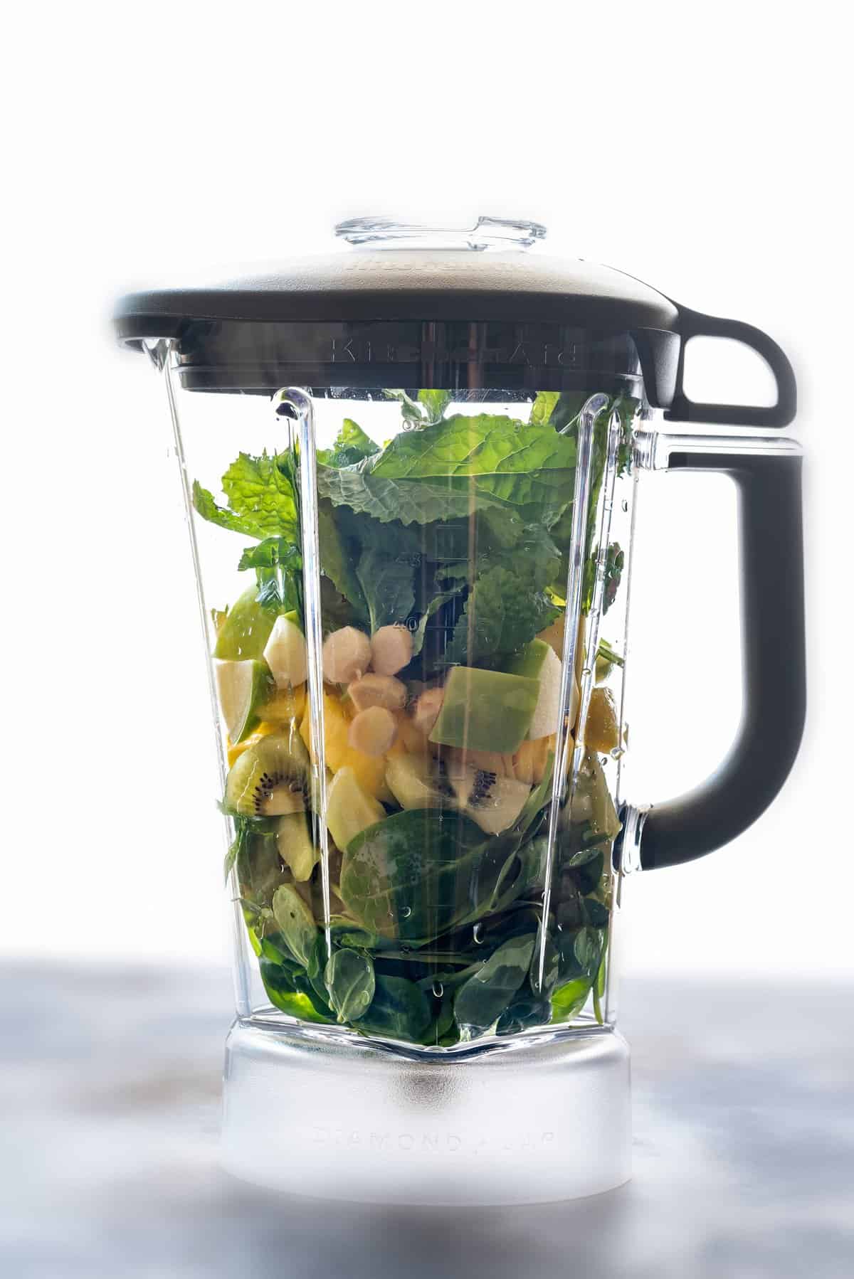 blender with kiwi, apple, mint, spinach, kale, ginger, lime juice, water, pineapple 