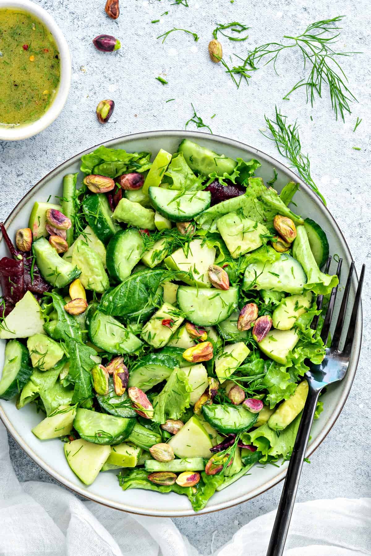 one bowl of mixed green salad with fresh dill and avocado with fork and dressing on side. 