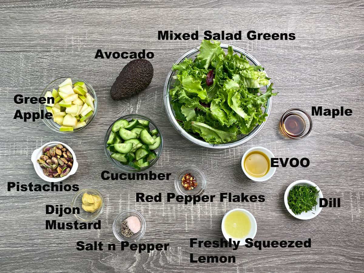 mixed greens, avocado, green apple, cucumber, pistachios and dressing ingredients prepared in bowls for salad.