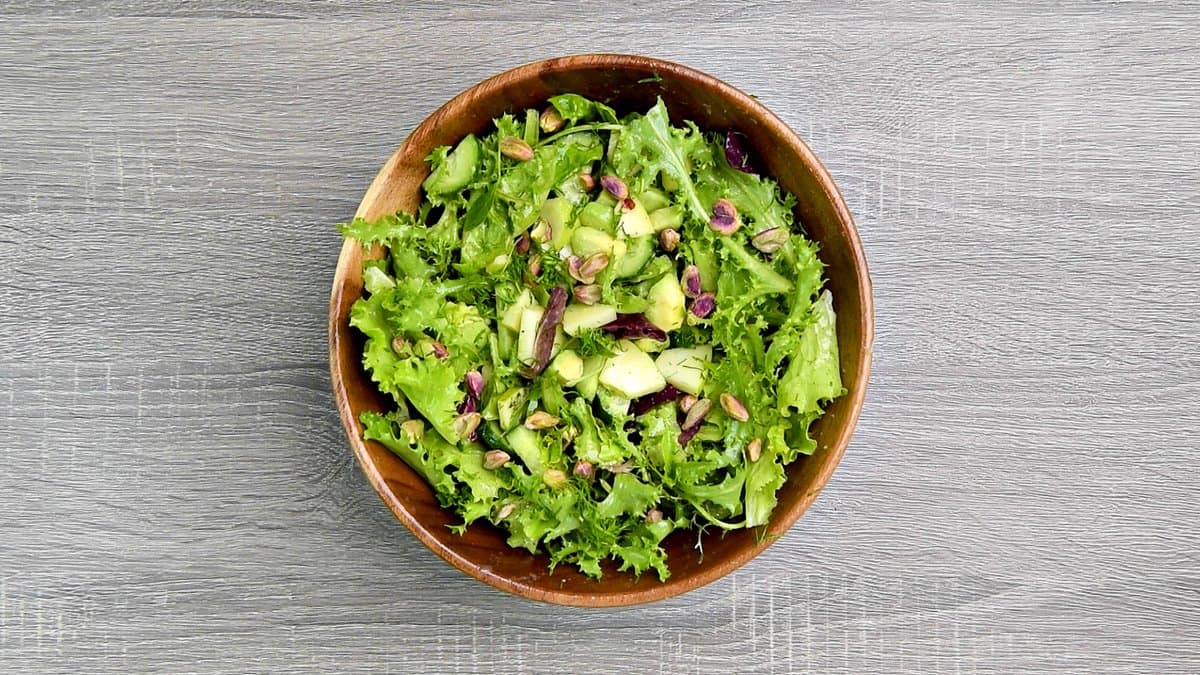 A wooden bowl with tossed mixed green salad and topped with pistachios.