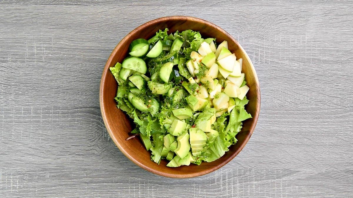 a wooden bowl with cucumbers, apples, mixed greens, avocado and lemon dill dressing.