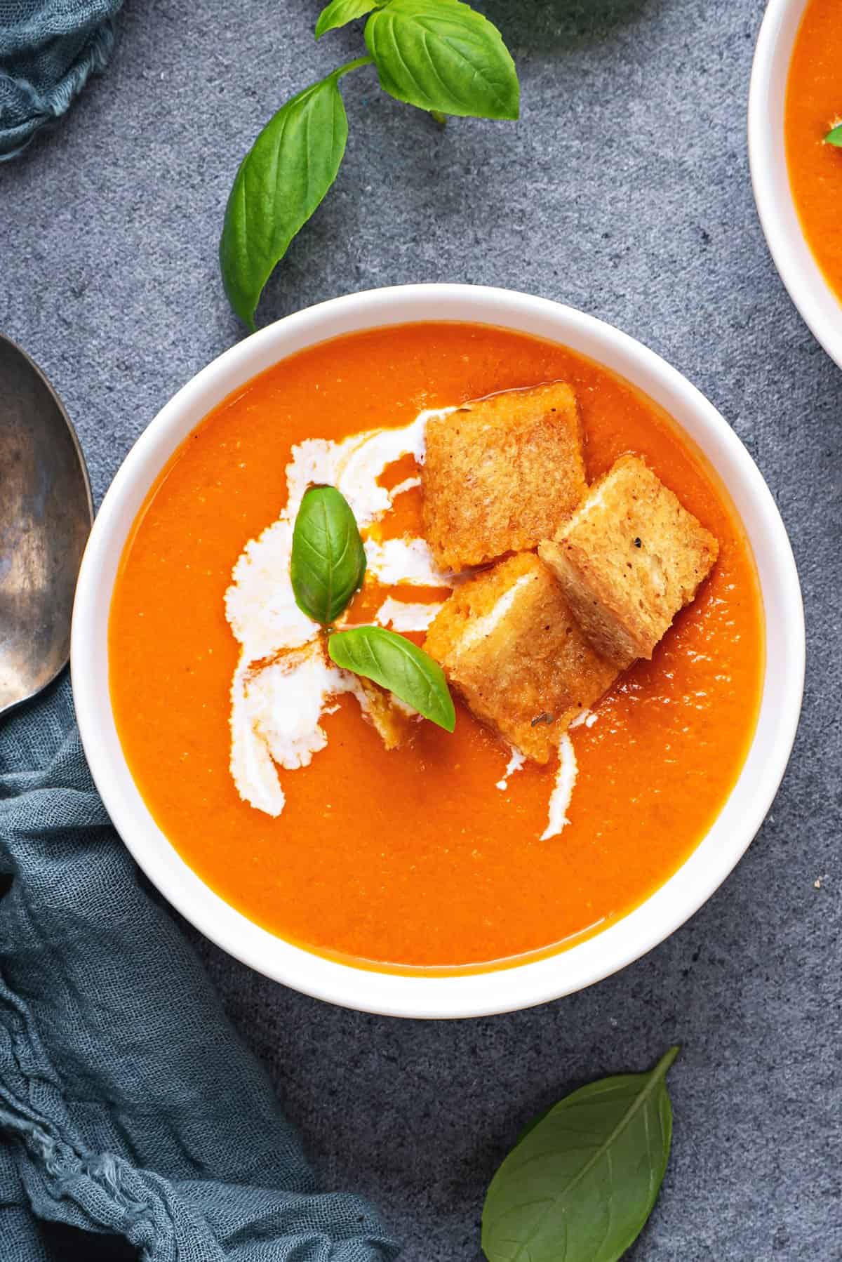 white bowl with tomato soup garnished with cream, fresh basil, and croutons 