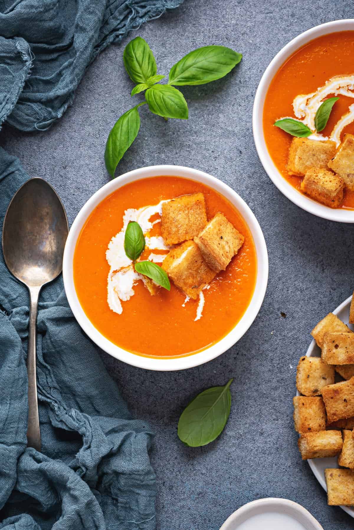two bowls of tomato soup with cream and fresh basil topped with croutons. 