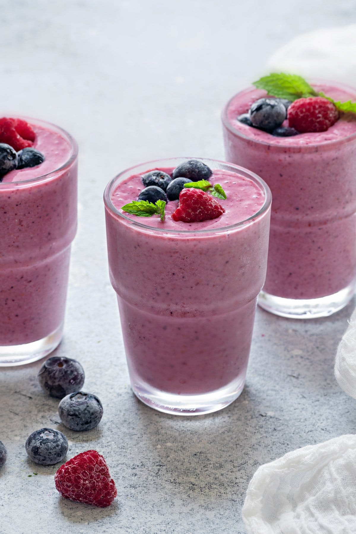 three glasses of mixed berry smoothies on grey table.