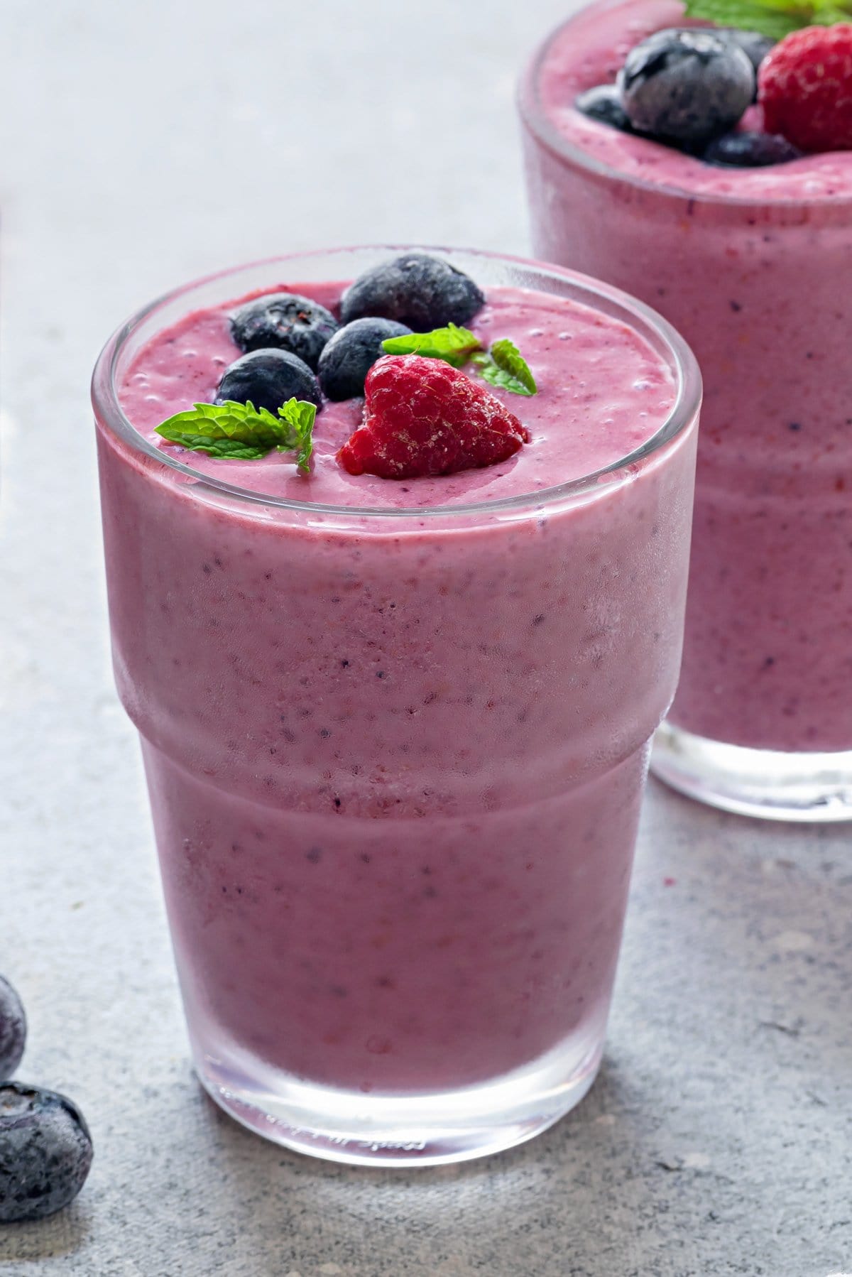 close-up of two glasses of mixed berry smoothies topped with berries and mint.