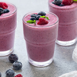 three glasses of mixed berry smoothies on grey table.