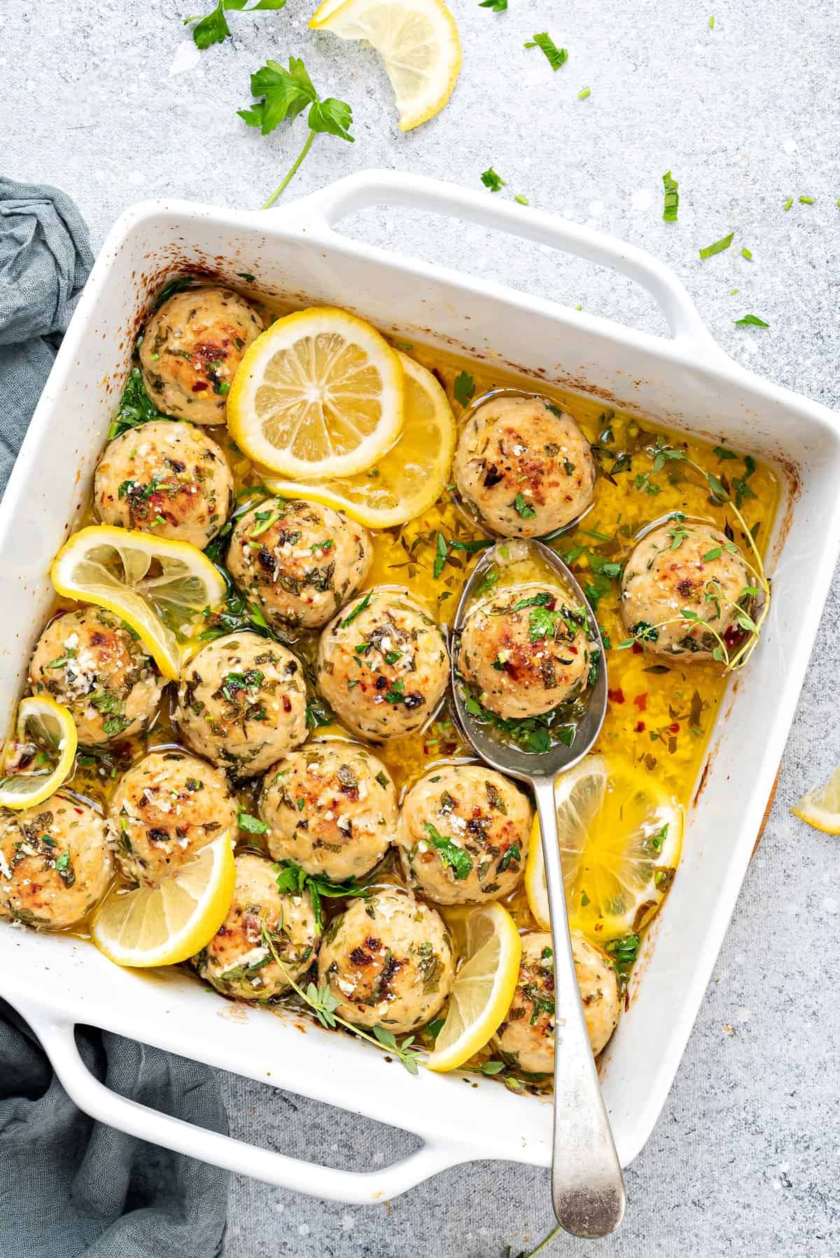Baked turkey meatballs in lemon butter sauce in a casserole dish with slices of lemon.  