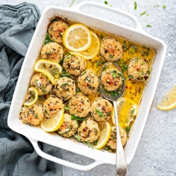 Baked turkey meatballs in lemon butter sauce in a glass casserole dish with one in a spoon.