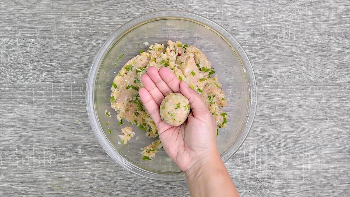 The mixture for the Turkey meatballs rolled into a 1 ½ inch ball in a hand over a glass bowl. 