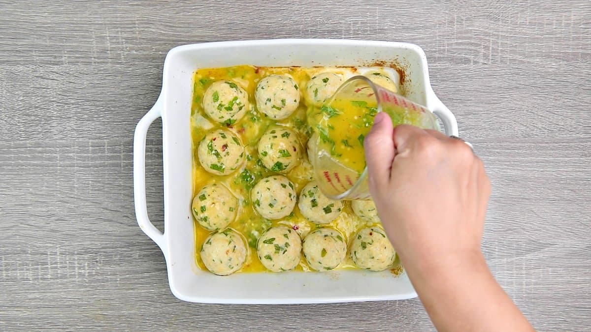 Pouring the lemon butter sauce from a cup into the turkey meatballs in the casserole dish. 