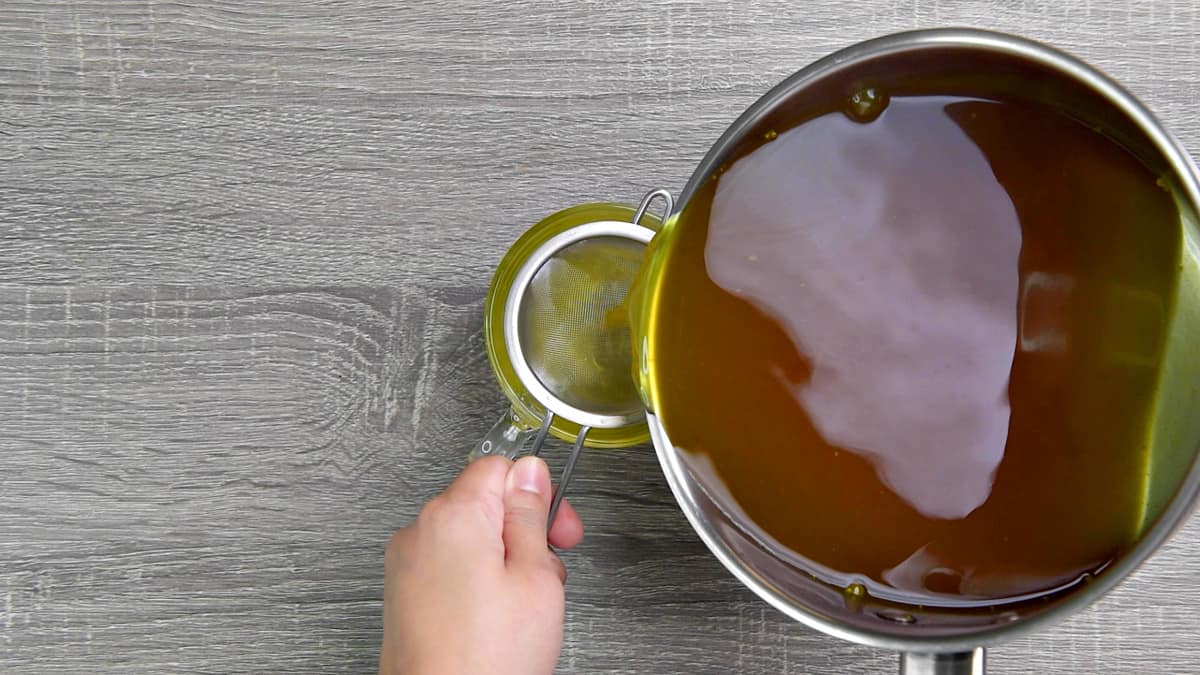 straining the ginger and turmeric herbal tea into a serving cup.