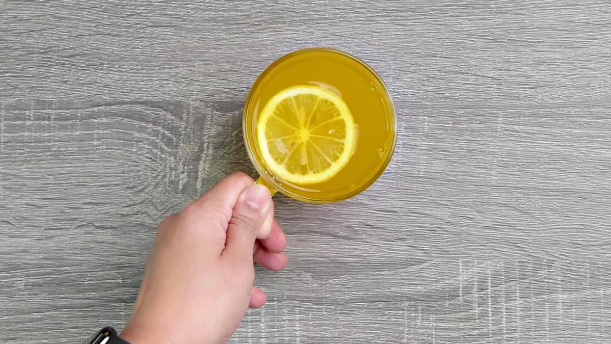 A hand holding a cup of ginger turmeric tea with honey, and lemon.