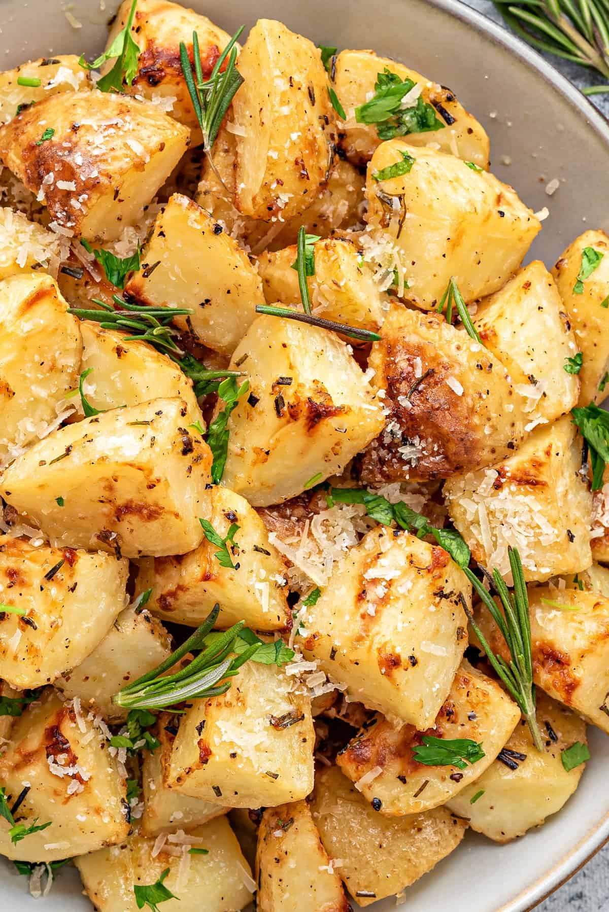 Close-up of parmesan rosemary roasted potatoes in a bowl garnished with fresh rosemary.