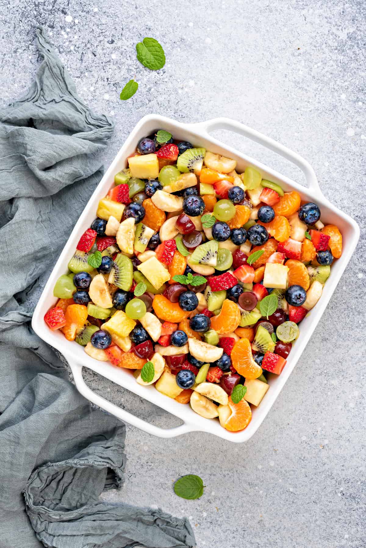 A white casserole dish with simple fruit salad garnished with fresh mint ready to serve.