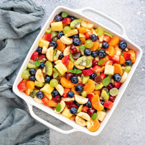 White casserole dish with simple summer fresh fruit salad garnished with fresh mint.