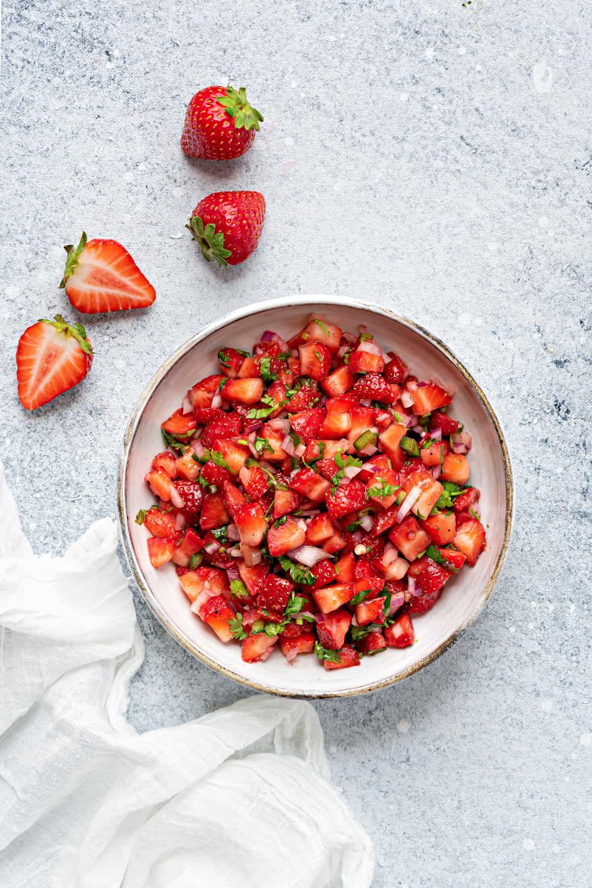 Fresh strawberry salsa serving in white ceramic bowl on white table.