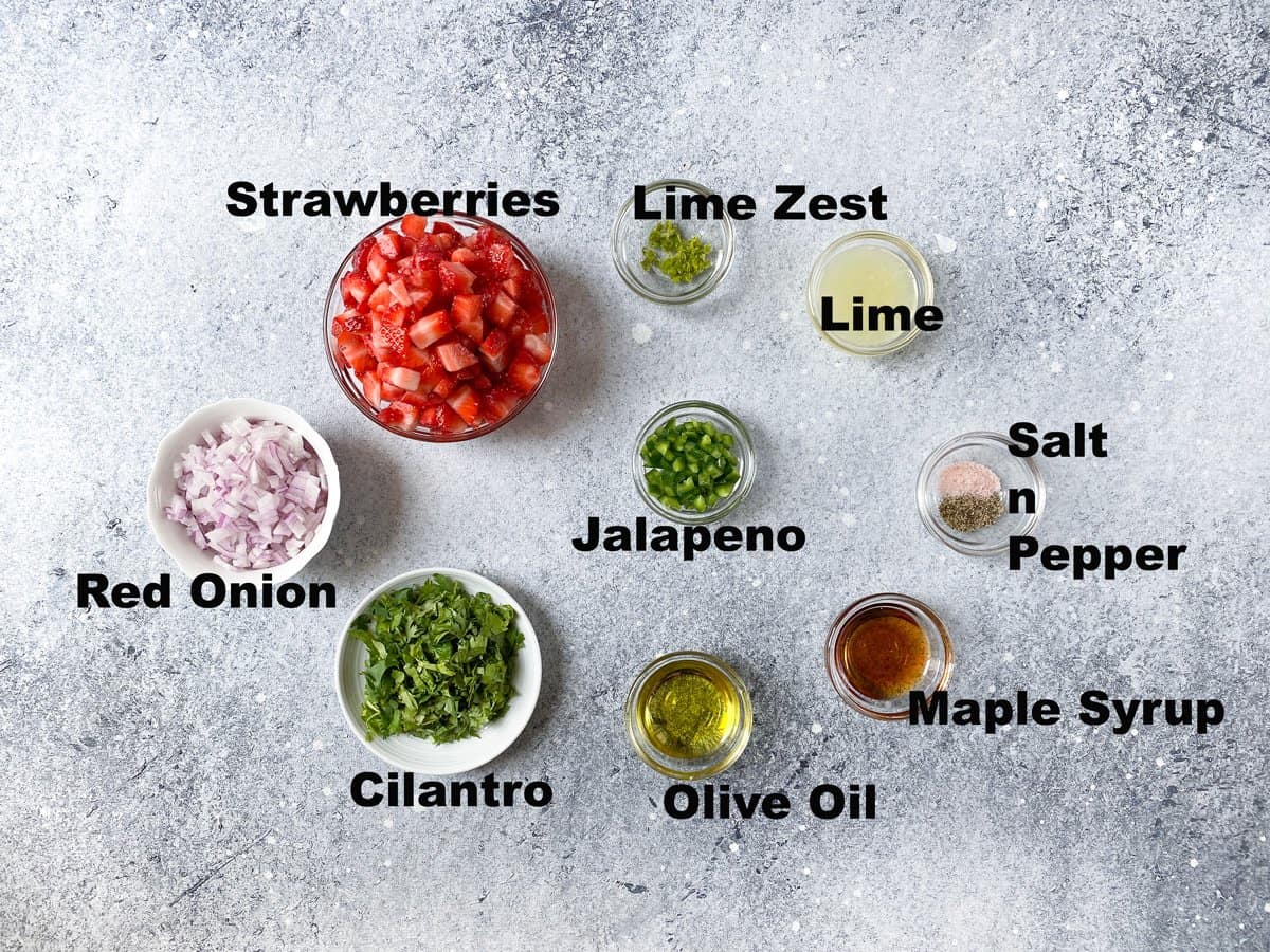 Ingredients for strawberry jalapeno salsa measured in small glass bowl on a white table.