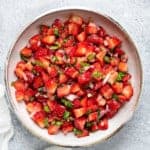 Fresh strawberry salsa serving in earthen bowl on a white table.