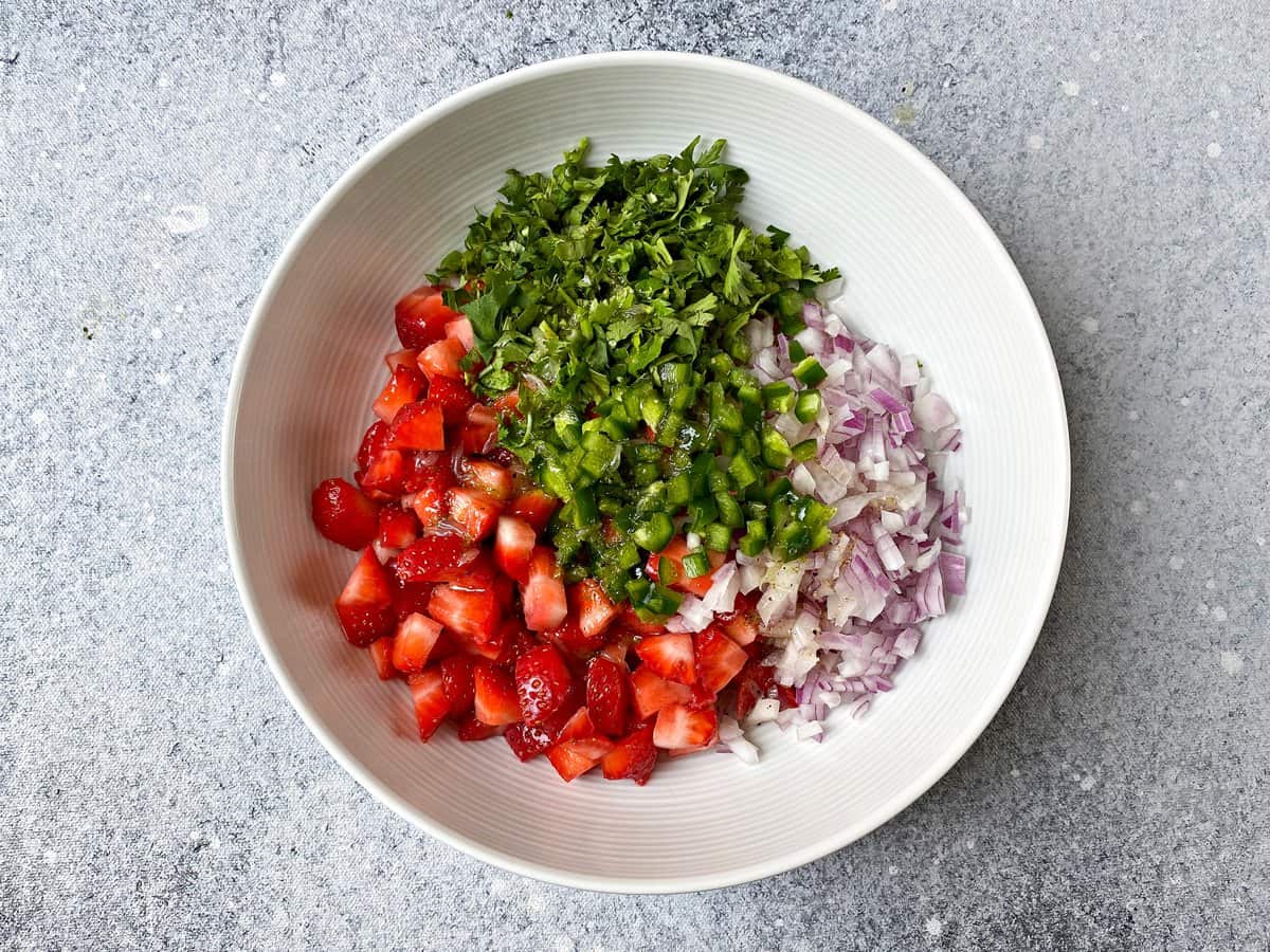 Chopped strawberries, red onion, jalapeno, cilantro and prepared dressing added in bowl.