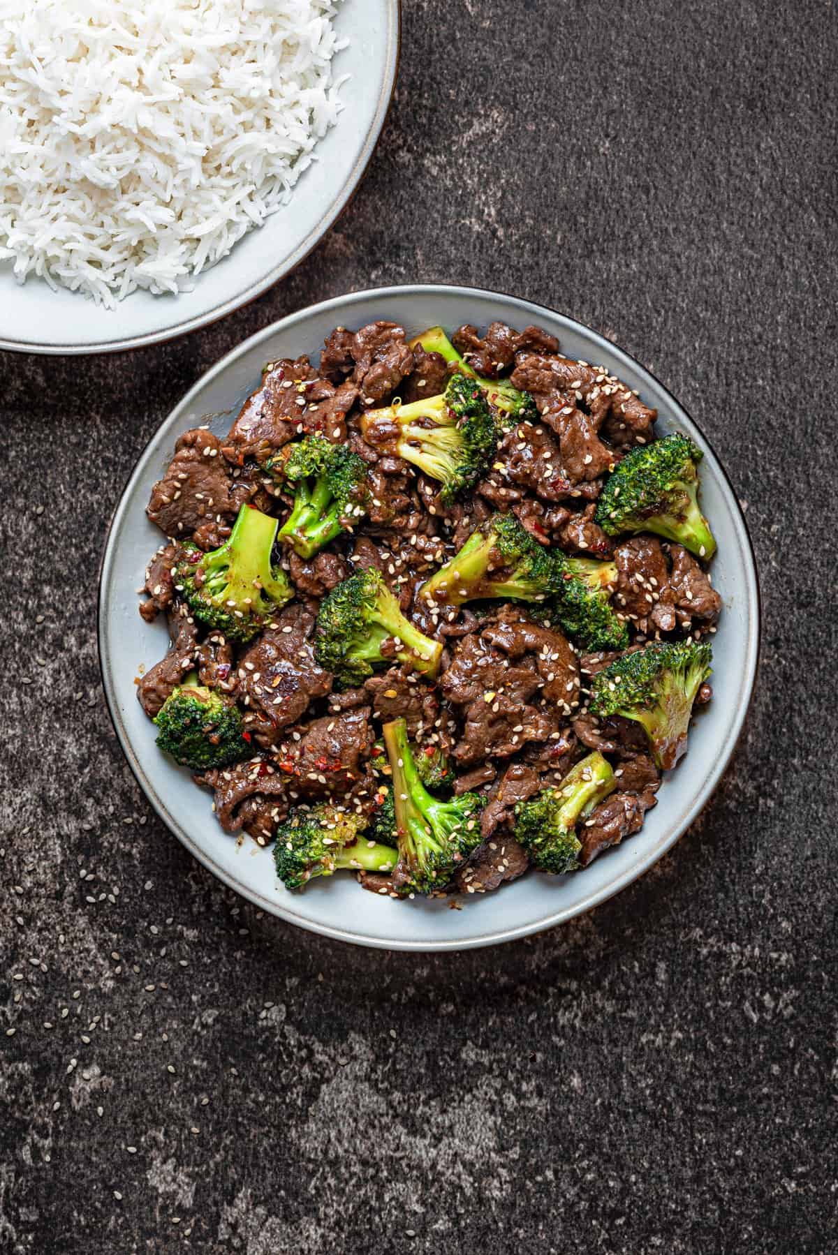 beef and broccoli in a grey bowl topped with red chili flakes and sesame seeds.