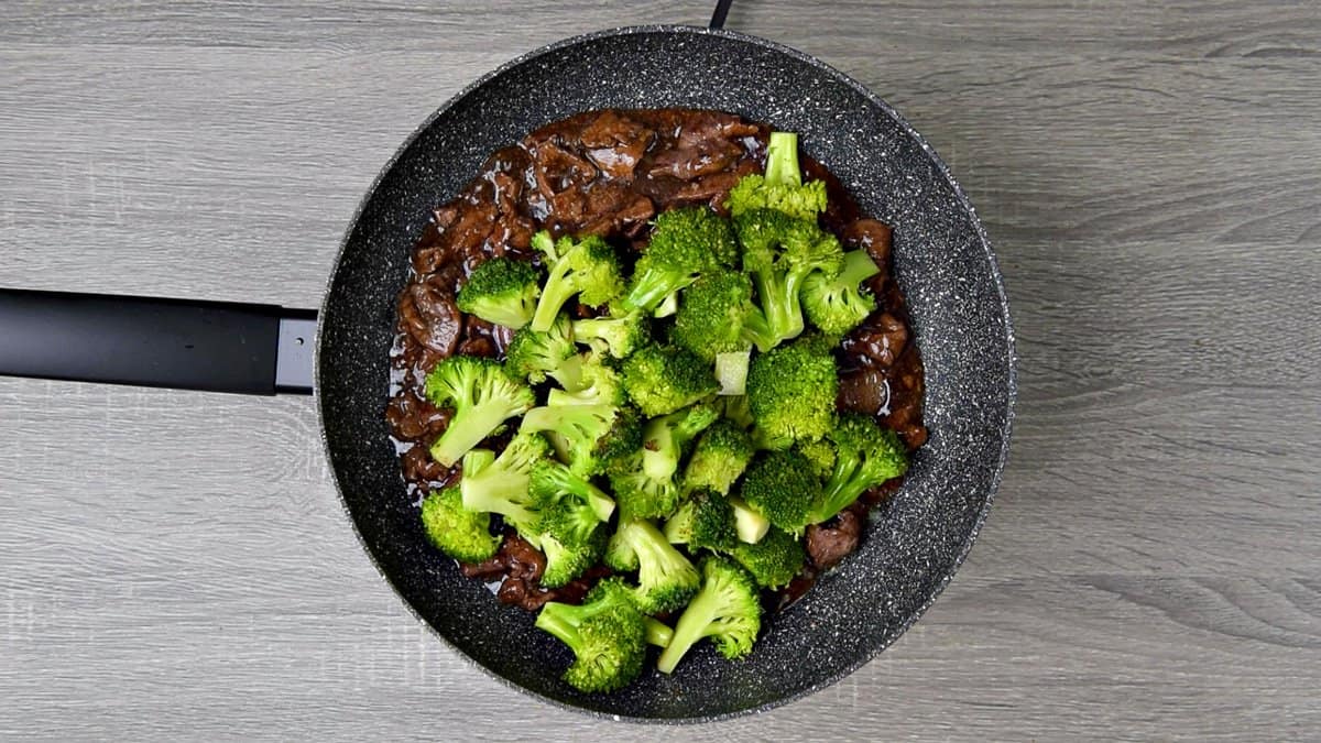 Sautéed broccoli florets added to skillet with cooked beef strips and sauce. 