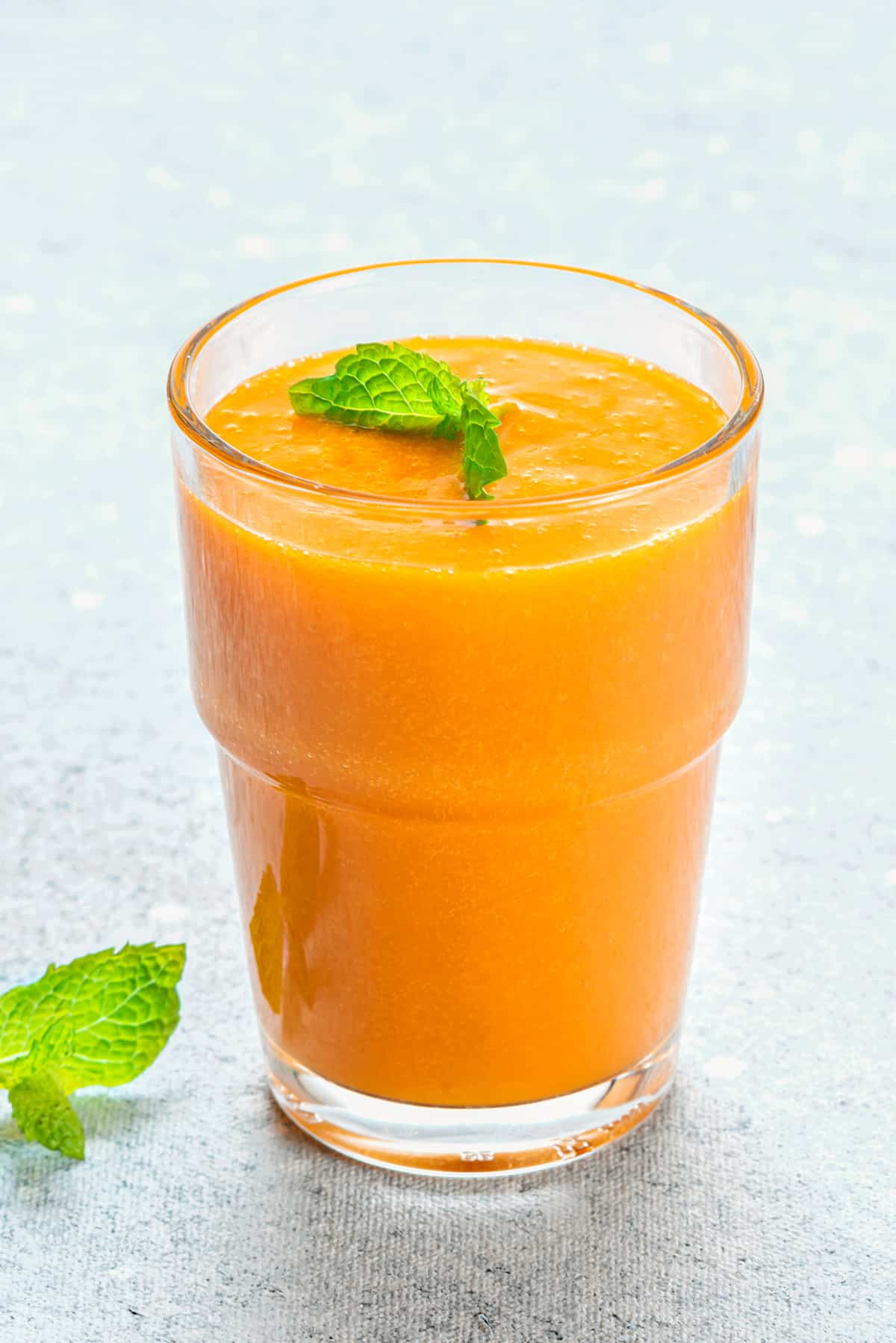Close-up of a glass filled with homemade mango nectar juice garnished with fresh mint.