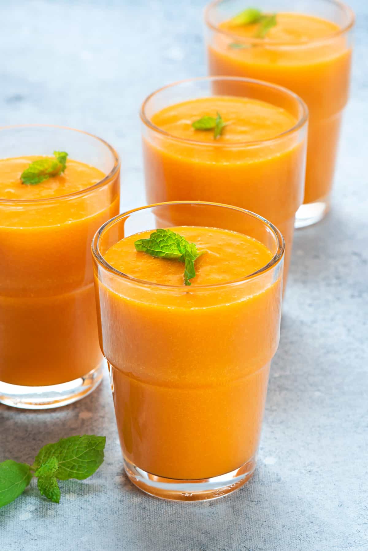 Four glasses with chilled fresh mango juice garnished with mint.