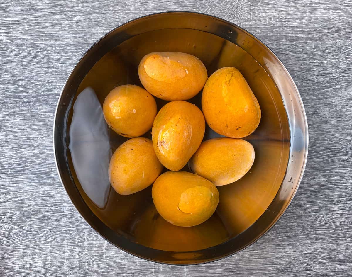 seven large sweet ripe mangoes soaking in water in large bowl.