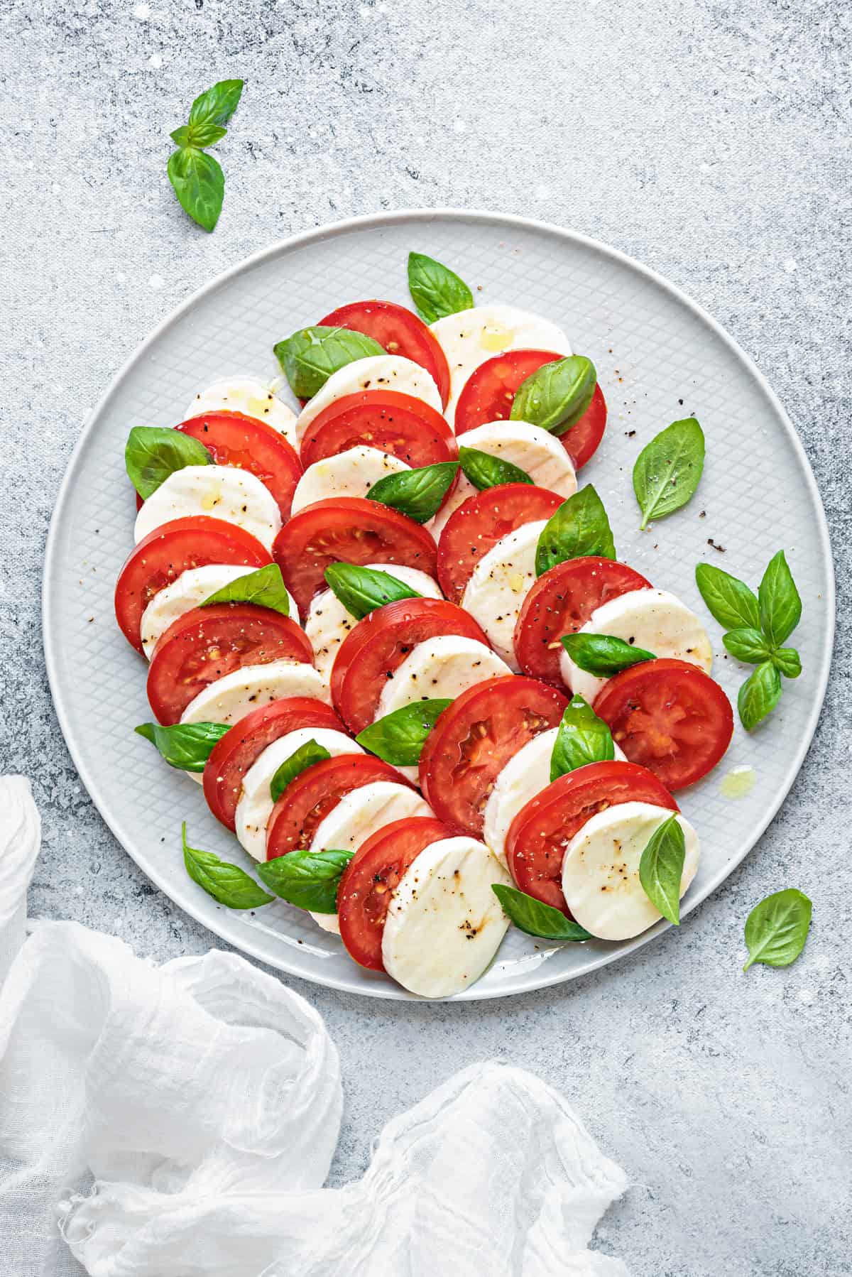 Top down view Caprese salad with tomato, mozzarella, and basil on a light gray plate.