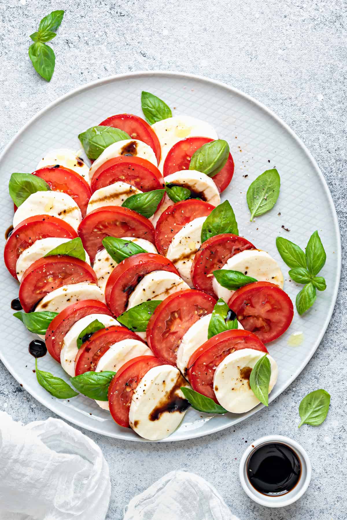 Close view gray plate with tomato mozzarella basil salad. White ramekin of balsamic glaze to the side.