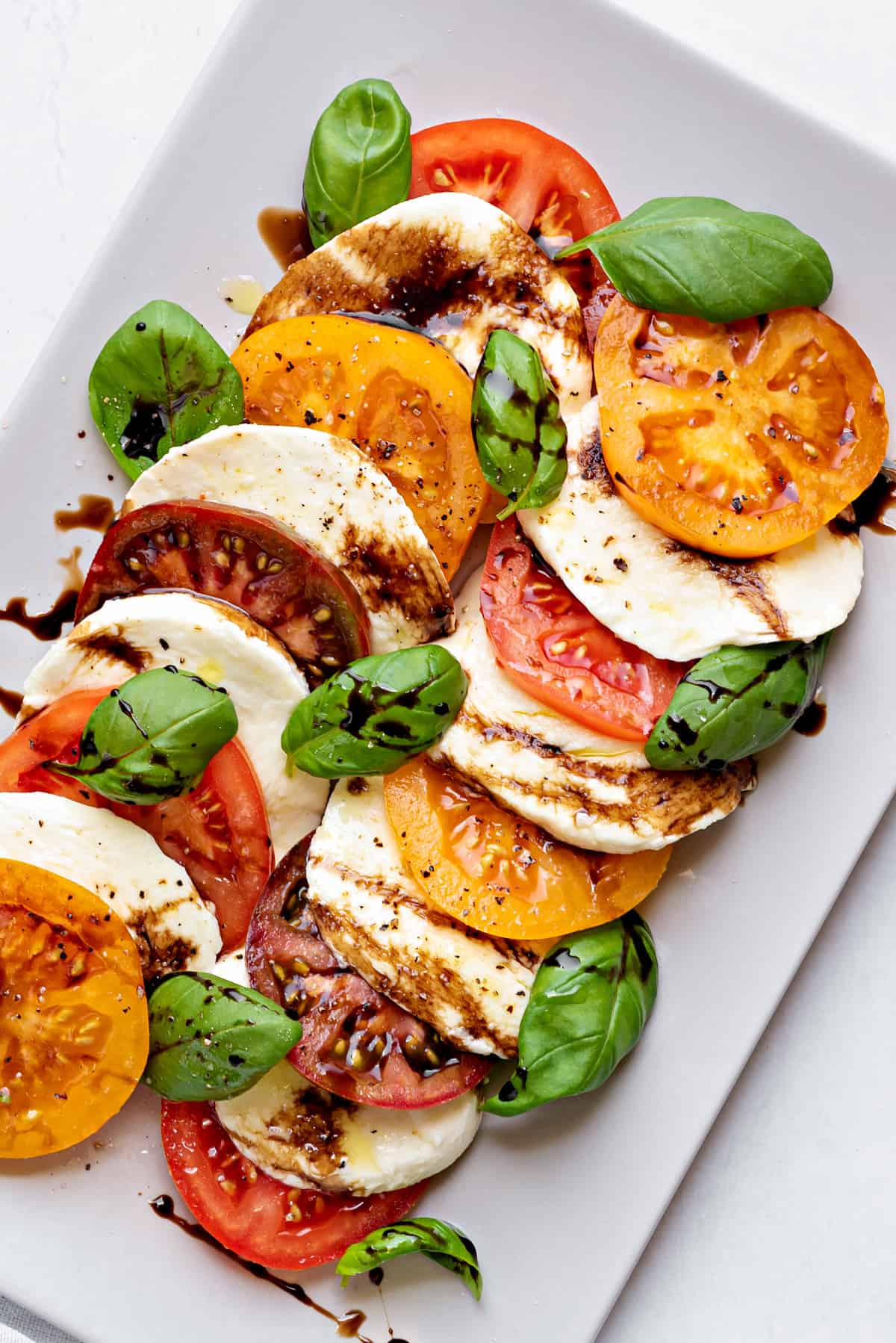 Two rows of layered Caprese salad on plate. Each row has layered tomatoes slices, mozzarella and basil.